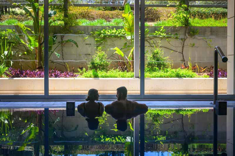 Couple looking at each other and enjoying the indoor pool with plants in the background at the Mallorca Wellness SPAs