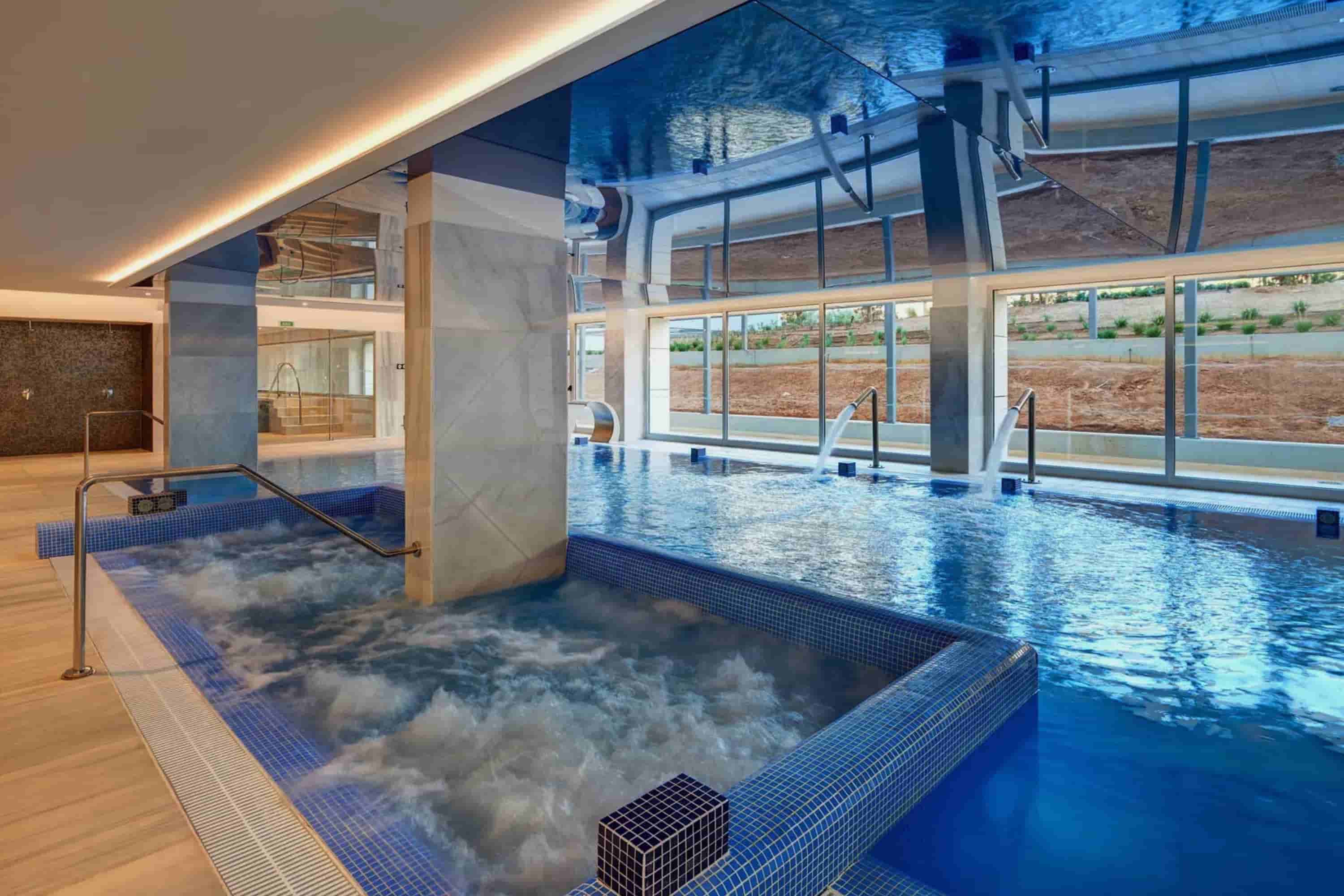 Indoor spa pool with jacuzzi, gooseneck water features and relaxation beds at Mallorca Wellness Spa – Gran Playa de Palma.